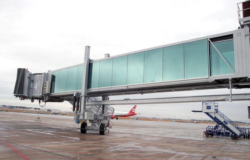 Glass-walled passenger boarding bridge connected to an aircraft gate.